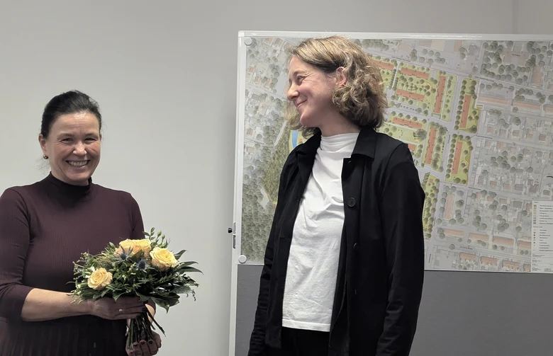 der Geschäftsführerin der Wobau Lauta wird ein Blumenstrauss übergeben; im Hintergrund sind Planungsunterlagen zu sehen