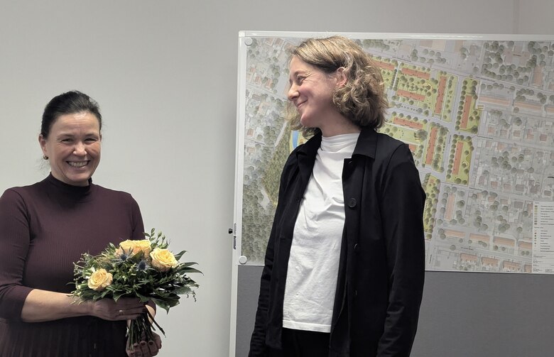 der Geschäftsführerin der Wobau Lauta wird ein Blumenstrauss übergeben; im Hintergrund sind Planungsunterlagen zu sehen