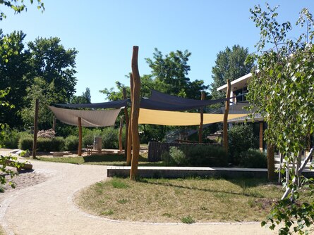 Sonnensegel an Holzpfählen in grüner Umgebung, um einem Spielbereich für Kinder Schatten zu schenken
