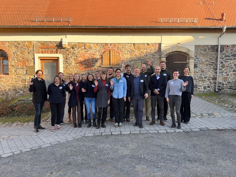 alle Teilnehmer als Gruppe versammelt winken in die Kamera