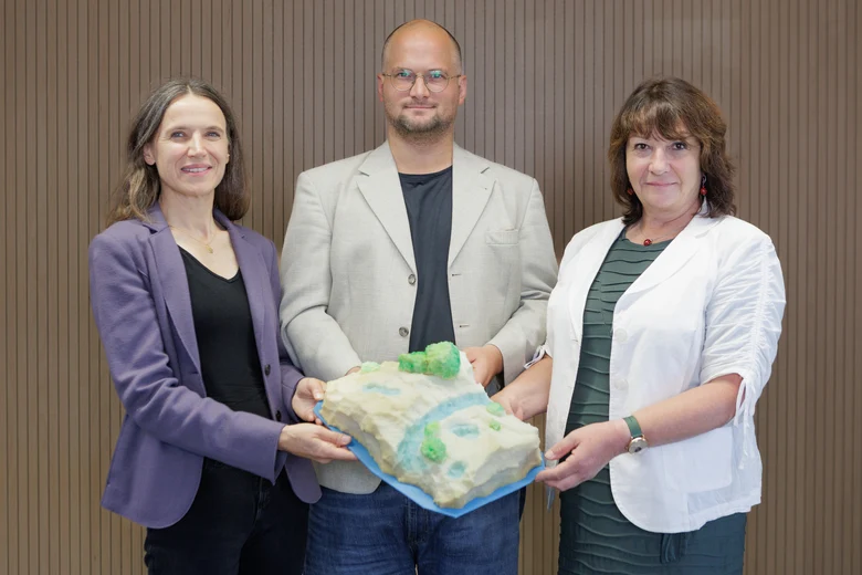 Zwei Frauen und ein Mann halten einen selbstgebastelten Preis hoch. Der Preis ist ein Schwamm der so zurechtgeschnitten ist, dass es wie eine Landschaft aussieht.