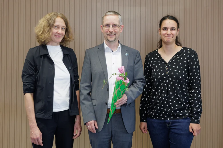 Zwei Frauen und ein Mann lächeln in die Kamera. Der Mann in der Mitte hält einen Preis in den Händen.
