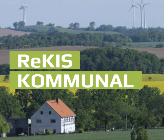 Schriftzug "ReKIS Kommunal" weiß auf hellgrünem Grund, links, dahinter ein Foto einer ländlichen Landschaft mit grünen Feldern und Bäumen, gelben Feld, Bauernhaus links und ganz hinten vor blauem Himmel Windräder