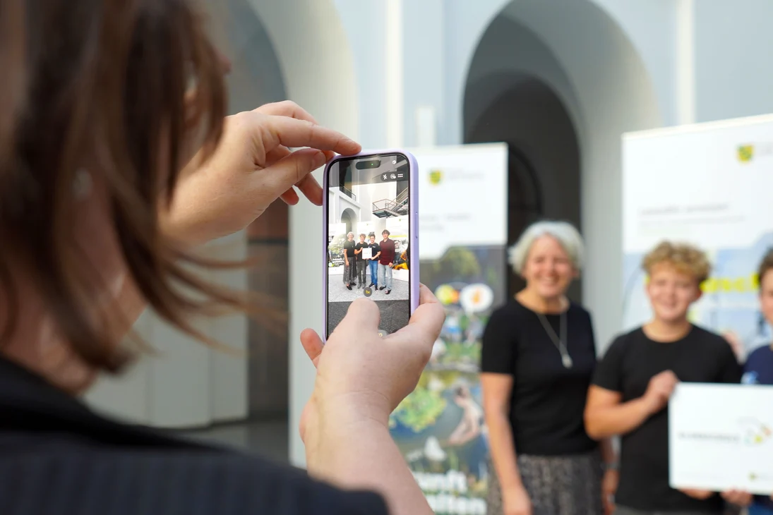 Eine ausgezeichnete Klimaschule wird mit dem Handy vor einem Klimaschulaufsteller fotografiert.
