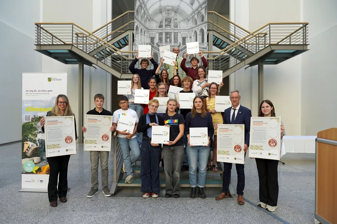 Je eine Vertreterin / ein Vertreter aller ausgezeichneten Klimaschulen stehen mit ihren Schildern und Urkunden auf der Treppe des Saals.